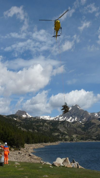 Hélicoptère avec charge suspendue survolant un lac de montagne