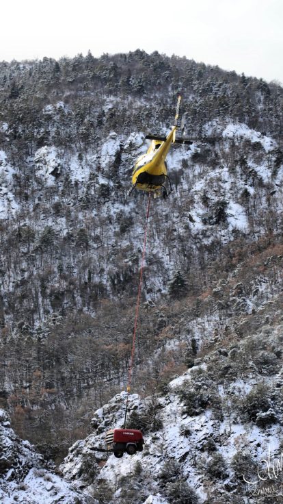 Hélicoptère survolant un pylône et une ligne haute tension sur une crête enneigée