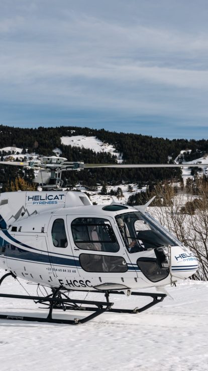 Hélicoptère posé dans la neige, station de ski et montagnes en arrière-plan