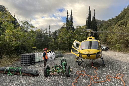 Hélicoptère posé sur l'herbe, équipe préparant un big bag relié à une élingue