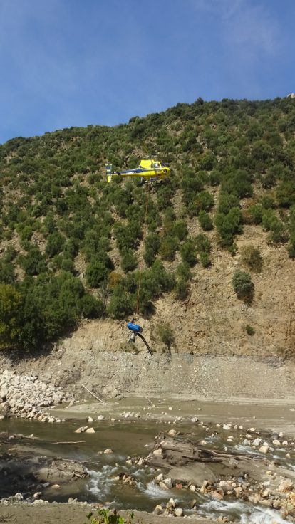Hélicoptère survolant un versant boisé au-dessus d'une rivière de montagne