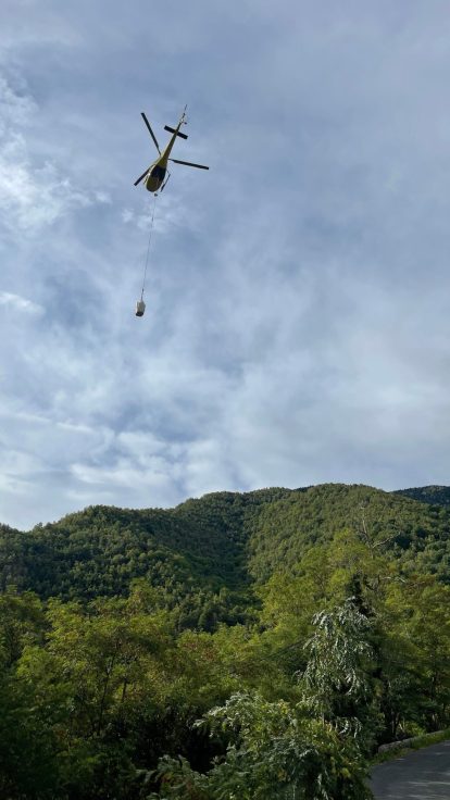 Hélicoptère tractant un câble au-dessus d'un versant montagneux enneigé