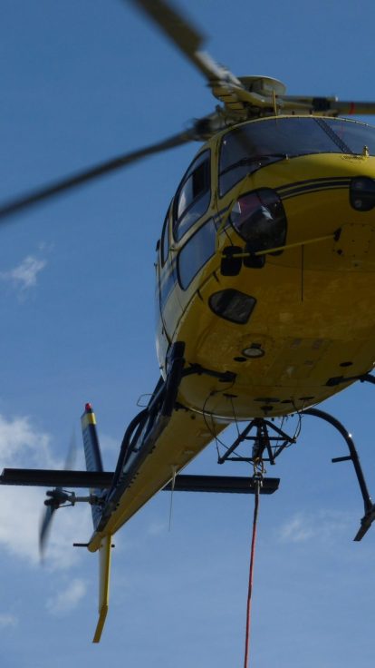 Vue de face de l'hélicoptère Hélicat en vol, longue élingue rouge suspendue