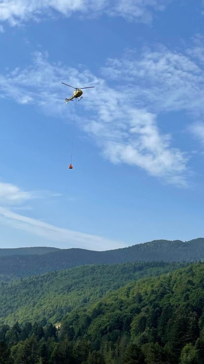 Hélicoptère survolant un chantier de haute montagne avec bétonnière au sol