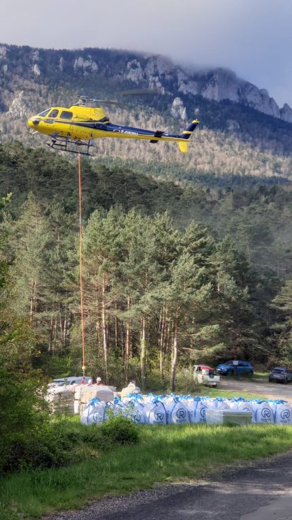 Helicopter carrying big bags of materials over a mountain forest