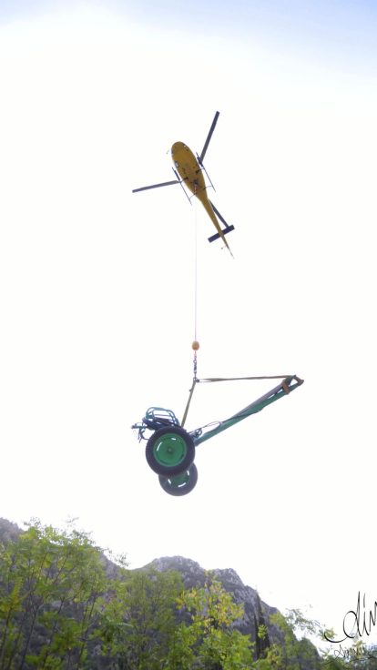 Hélicoptère treuillant un chariot à roues au-dessus d'une paroi rocheuse