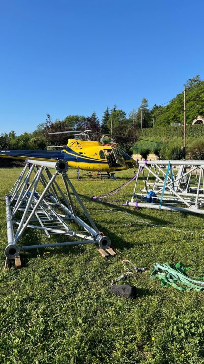 Hélicoptère transportant un élément métallique au-dessus d'une colline fleurie