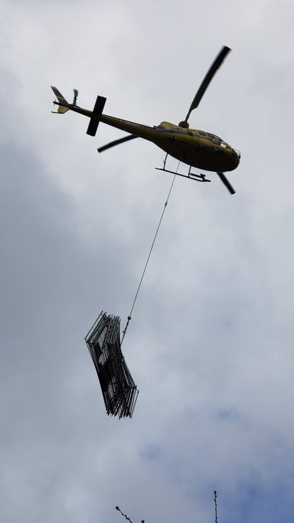 Hélicoptère héliportant une structure métallique grillagée, ciel nuageux